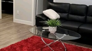 A modern living room with a black leather sofa, a glass coffee table with a plant, and a red rug.
