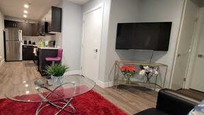 A modern living space with a glass dining table, a red rug, a sofa, a TV, and a kitchen in the background.