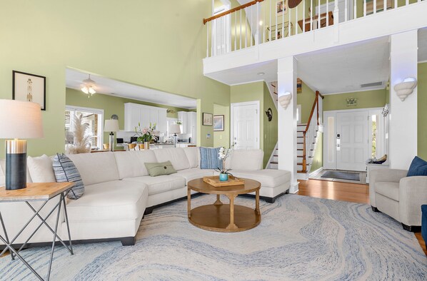 A spacious living room with a sectional sofa, a coffee table, and a staircase leading to an upper level. - Dolphins Folly | Oceanfront Home with Private Beach Access, Ocean Views & Multiple Decks (Folly Beach)