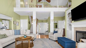 Un vaste salon doté d’un haut plafond, d’une cheminée et d’un escalier menant à un niveau supérieur.