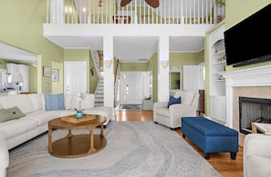 A spacious living room with a high ceiling, a fireplace, and a staircase leading to an upper level.
