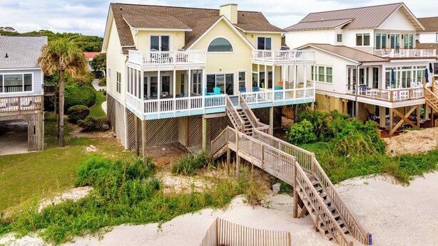 Une propriété située en bord de mer, dotée de plusieurs terrasses et d’un escalier en bois menant à la plage.