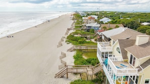 Une propriété située en bord de mer, avec une passerelle en bois menant à un balcon doté d’un espace salon extérieur.