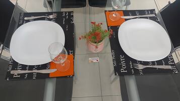 Une table à manger dressée avec de l’assiette blanche, des couverts et des verres à vin, ainsi que des sets de table assortis et une petite plante en pot.