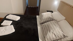 A neatly made bed with white and striped pillows, a black bedspread, and three white towels on the side. - What you were looking for in Nueva Cordoba (Córdoba)