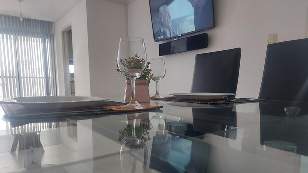 A modern dining area with a glass table, two wine glasses, a potted plant, and a laptop on the table. - What you were looking for in Nueva Cordoba (Córdoba)