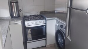 A compact kitchen with a gas stove, oven, washing machine, and a refrigerator. - What you were looking for in Nueva Cordoba (Córdoba)