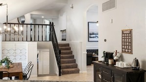Uma cozinha moderna com bancada de granito, um espaço de refeições com mesa e cadeiras de madeira, uma escada que leva a um andar superior e uma sala de estar com sofá e mesa de centro.