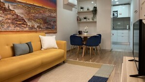 Een woonkamer met een gele bank, een eettafel met stoelen, een televisie en een schilderij aan de muur.