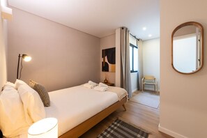 Una habitación de hotel moderna con una cama grande, una lámpara de noche, una mesita y un espejo.