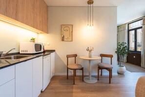 Eine moderne Küche mit Mikrowelle, Spüle und Holzschränken. Ein runder Tisch mit zwei Stühlen und eine Blumenvase stehen bereit. Ein Bild hängt an der Wand, und eine Pflanze steht in der Ecke.