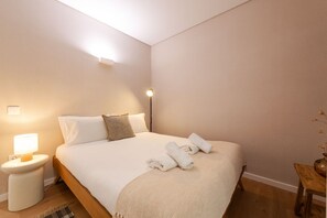 Ein Schlafzimmer mit einem Bett, einem Nachttisch, einer Lampe und einem kleinen Holzhocker.