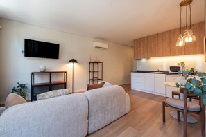 Un apartamento moderno con sofá, televisor de pantalla plana, kitchenette y zona de comedor.
