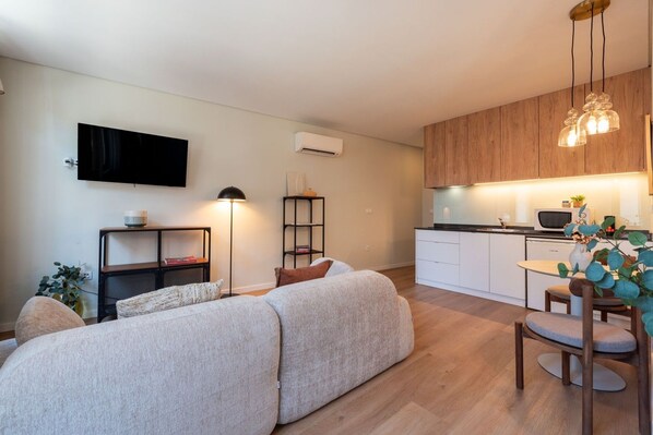 Un apartamento moderno con sofá, televisor de pantalla plana, kitchenette y zona de comedor.