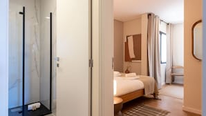 A hotel room with a glass shower, a bed with a headboard, a window with curtains, and a mirror on the wall. - Bright Apartment Next to D. Luis Bridge by Lisbeyond (Vila Nova de Gaia)