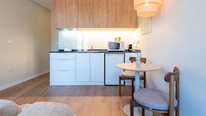 A compact kitchen with wooden cabinets, a microwave, a small refrigerator, and a round dining table with two chairs. - Bright Apartment Next to D. Luis Bridge by Lisbeyond (Vila Nova de Gaia)