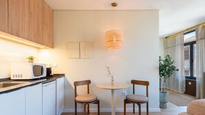 A modern kitchen with a microwave, two chairs, a round table, and a hanging light fixture. - Bright Apartment Next to D. Luis Bridge by Lisbeyond (Vila Nova de Gaia)
