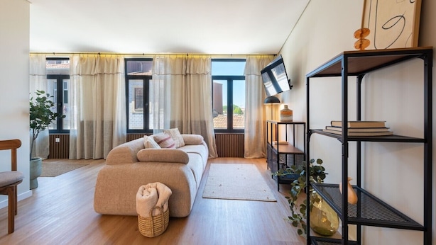 A modern living room with a sofa, a bookshelf, and a view through large windows. - Bright Apartment Next to D. Luis Bridge by Lisbeyond (Vila Nova de Gaia)
