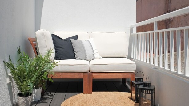 Un'area relax esterna con un divanetto di legno, due cuscini bianchi e un piccolo tappeto.