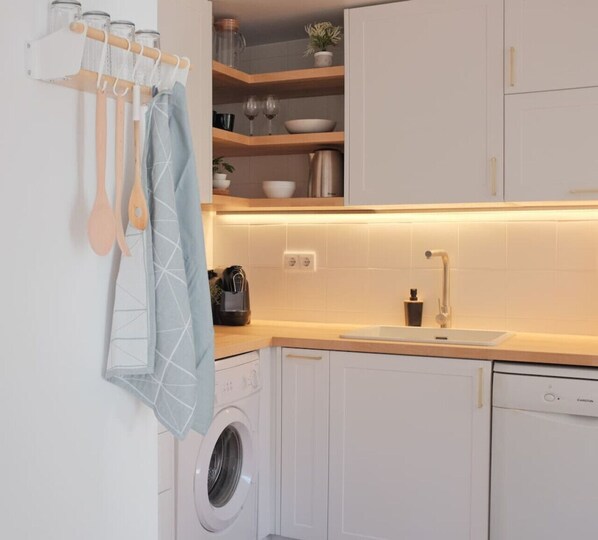 A compact kitchen with a washing machine, a sink, and wooden shelves above. - Terrace in Downtown Graça | With a private terrace! (Lisboa)