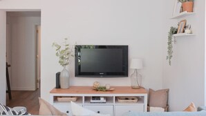 Un soggiorno moderno con una televisione a schermo piatto montata su una consolle in legno, un vaso con foglie verdi e una mensola a parete con piante e libri.
