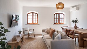 Un soggiorno moderno con divano, poltrone, un tavolo da pranzo e due finestre con stipiti in legno.