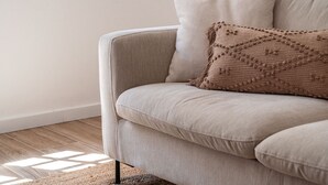 Un divano beige con un cuscino decorativo e un cuscino semplice, su uno sfondo neutro.