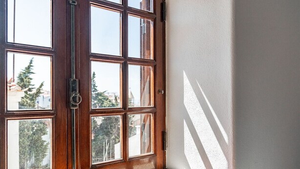 Una finestra con stipite in legno, diversi vetri, una maniglia metallica e un piccolo davanzale in legno sotto.