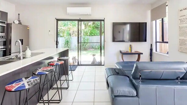 Una cocina moderna con una isla central, un comedor con taburetes de bar, un sofá y un televisor montado en la pared.