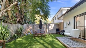 Un patio trasero con una terraza de madera, una mesa de comedor y un sofá blanco.