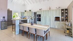 Una cocina moderna con una isla central, electrodomésticos integrados y una zona de comedor con una mesa grande y sillas.