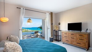 Un dormitorio con una cama grande, televisión, cómoda de madera y vista al océano.