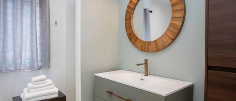 Un baño con un espejo redondo, lavamanos blanco y un mueble de madera.