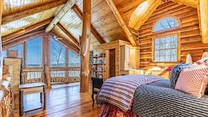 A log cabin bedroom with a large bed, wooden walls, and a view of the outdoors. - Beautiful Rustic Lakehouse in Michigan, gorgeous views and total relaxation (Montgomery)