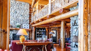 A spacious log cabin interior with a high ceiling, wooden floors, a stone wall, and a cozy seating area with a fireplace. - Beautiful Rustic Lakehouse in Michigan, gorgeous views and total relaxation (Montgomery)