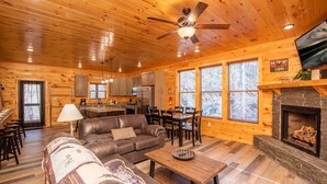 Un interior de cabaña con sala de estar, comedor, cocina y chimenea.