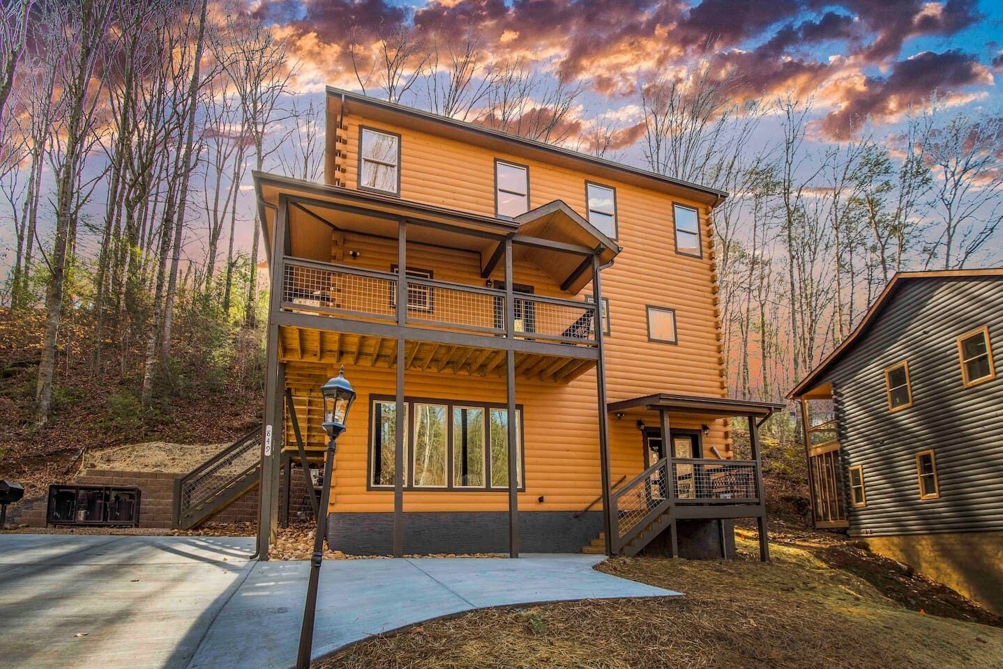A two-story log cabin with a balcony and a small porch, surrounded by trees.