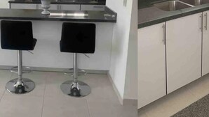 A modern kitchen with two black bar stools, a stainless steel sink, and white cabinets. - CONDOS AA (Mazatlán)