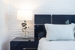 A modern bedroom with a bed, a nightstand, and a wall-mounted lamp. - Blue Heaven - Luxe Ocean Villa - Beach House - Private Pool (Melbourne Beach)