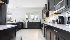 A modern kitchen with dark cabinetry, a stainless steel sink, and a large window providing natural light.