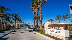 A sign for Harbor Island Beach Club with a clear pathway and palm trees.