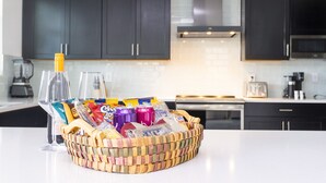 A kitchen with dark cabinets, a white countertop, and a wicker basket containing snacks and drinks.