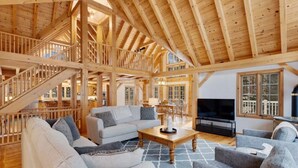 Un intérieur spacieux en bois, avec un escalier, un coin salon doté de canapés et d’une table basse, ainsi qu’un téléviseur.
