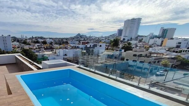 A rooftop pool with a cityscape view, including a prominent building in the distance. - Condos FRP (Mazatlán)