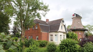 A traditional brick house with a thatched tower, surrounded by lush greenery.