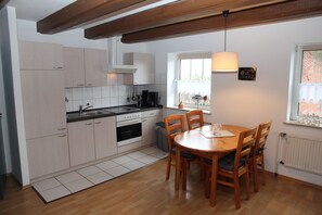 Une cuisine compacte avec des meubles blancs, une table à manger en bois et un luminaire suspendu.