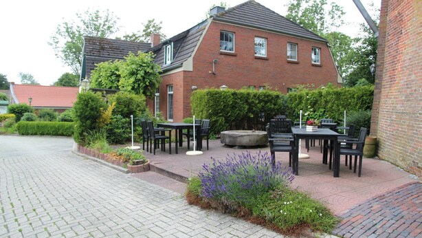 A brick house with a garden patio area featuring outdoor seating and a fire pit.