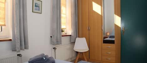 Un dormitorio con cama, una silla, un armario y una ventana con cortinas.