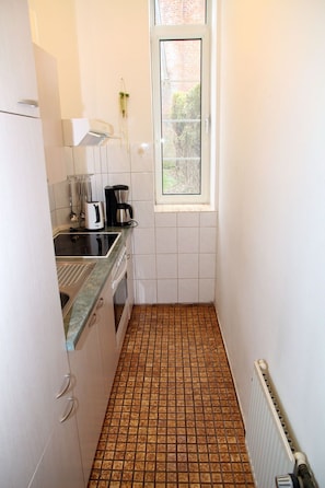 Cocina compacta con armarios blancos, encimera negra, cafetera y ventana con vista a zonas verdes.