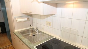 Een keuken met een roestvrijstalen spoelbak, een inbouwfornuis met vier branders, en een klein aanrecht.